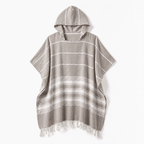 Formeya Poncho in Kaffeebraun. Eine Person entspannt damit auf einem gemütlichen Sofa zu Hause.