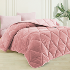 Rosa Wellsoft-Steppdecke mit Rautenmuster auf einem Bett, dazu passende Kissen. Im Hintergrund eine weiße Wand und Pflanze.