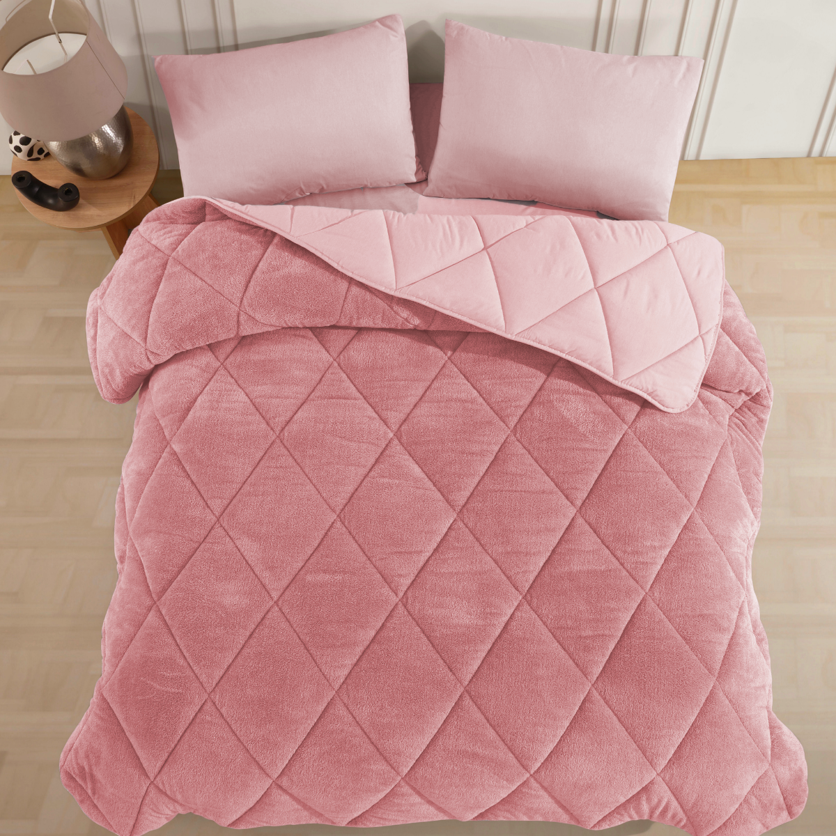 Rosa, gesteppte Wellsoft-Steppdecke auf einem Bett mit zwei Kissen. Die flauschige, doppelseitige Decke hat ein Rautenmuster.