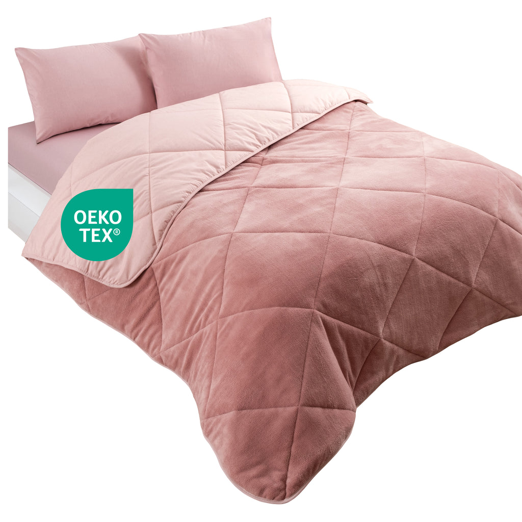 Ein Bett mit einer rosafarbenen, gesteppten Wellsoft-Decke und zwei passenden Kissen, mit OEKO-TEX Logo.