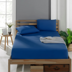 Baumwoll Spannbettlaken: Dunkelblaues Laken auf einem Holzbett mit zwei Kissen und einem aufgeschlagenen Buch.