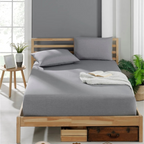 Spannbettlaken Baumwolle: Ein Bett mit grauem Spannbettlaken, zwei Kissen und einer Decke in einem hellen Schlafzimmer.
