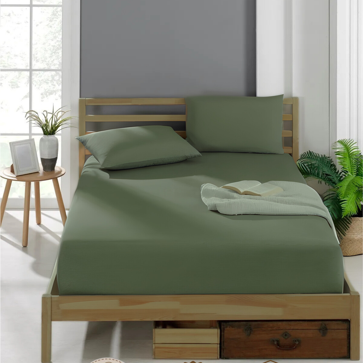 Spannbettlaken Baumwolle - Ein Bett mit olivgrünem Spannbettlaken, zwei Kissen und einer Decke mit Buch. Daneben ein